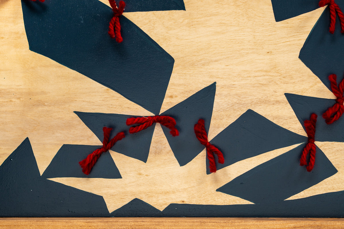 Detail of Quilt by Sydney Noland: the bottom edge of the painting, with red yarn ties and natural wood stars against deep blue