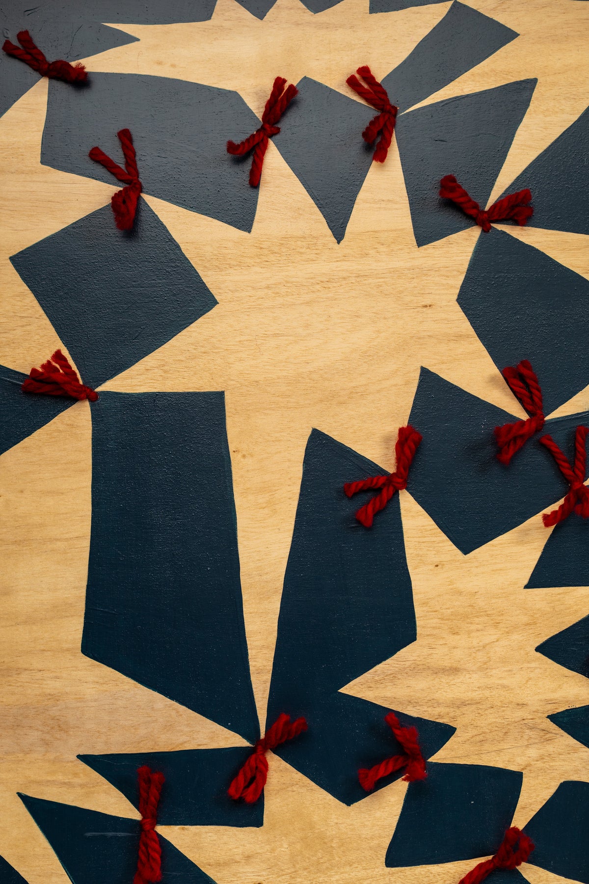Detail of Quilt by Sydney Noland: a vertical section of deep blue geometric shapes and wood star forms joined with red yarn